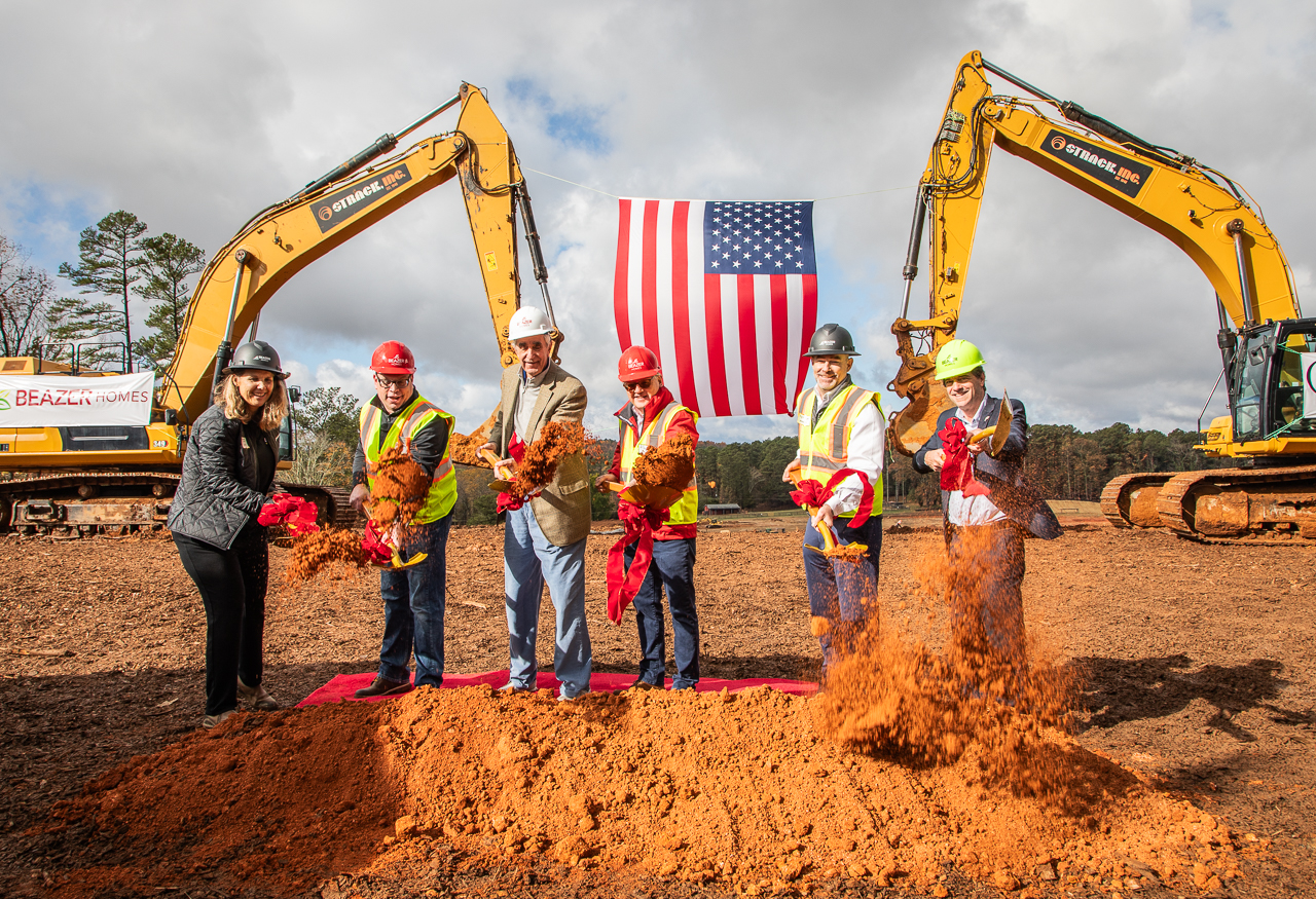 6 people stand with hard hats and shovels to break ground on a ne community of homes